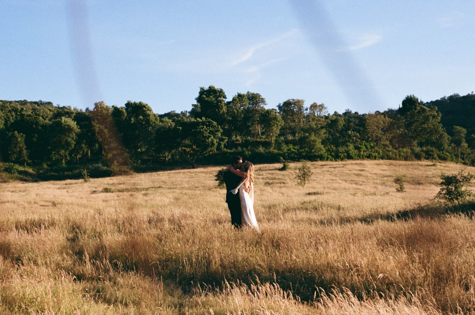 A bride and groom embracing in a golden meadow at sunset